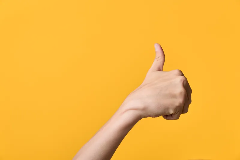 Hand, thumbs up gesture against a yellow background, signaling approval and positive feedback in a simple, clean shot suitable for success, encouragement, and user experience contexts