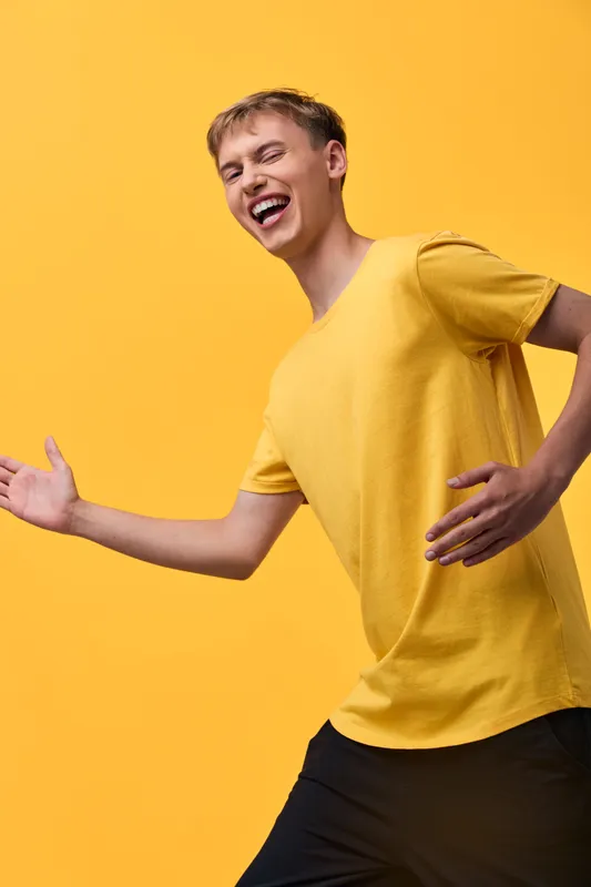 Joyful man in a bright yellow shirt laughs with energetic movement in a studio, conveying cheerful mood, bold color, and positive style for lifestyle or fashion projects