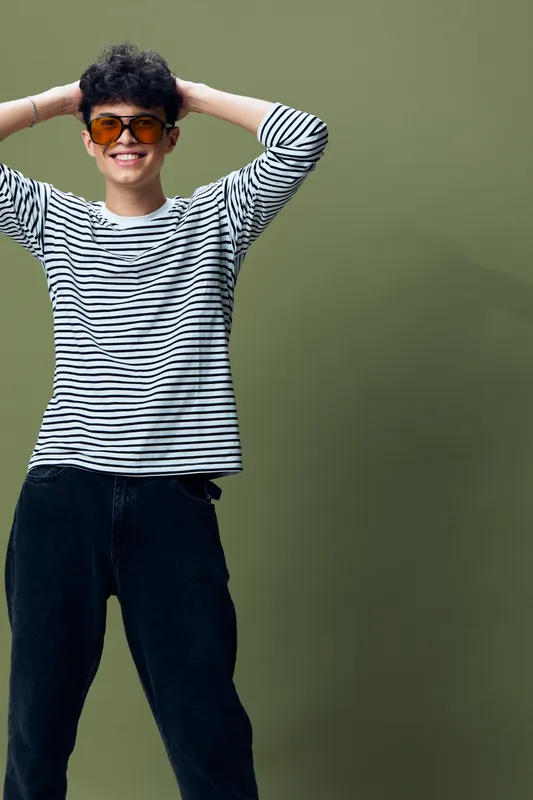 smiling young man wearing striped shirt and orange sunglasses posing confidently against green background with casual relaxed posture and short curly hair