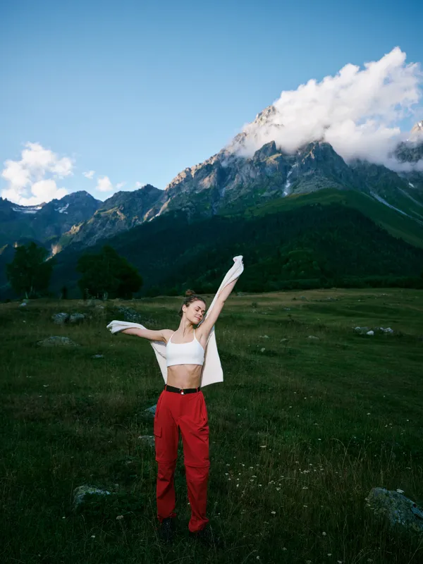 Female dancer in a meadow under a blue sky with alpine mountains, expressing freedom and joy through movement and light, outdoor scenery and energetic posture with a vivid mood and vast natural