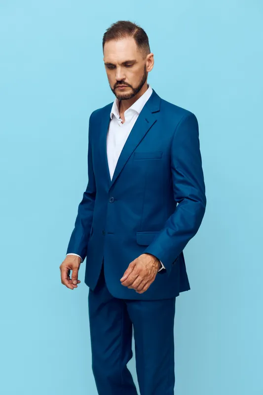 A focused business professional stands against a solid blue backdrop, exuding confidence and calm. He wears a sharp suit, expressing determination and readiness for a new challenge.