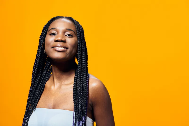 Smiling young Black woman with braided hair on a vibrant yellow background, showcasing confidence and joy in a spring summer fashion style
