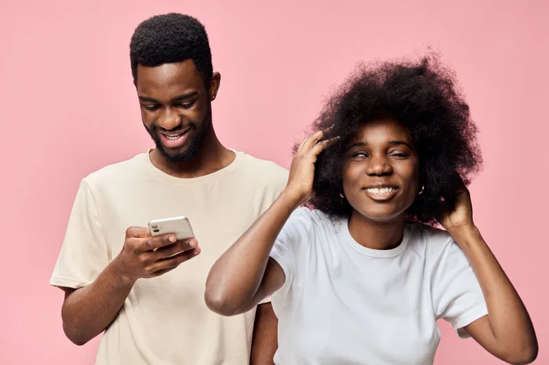 Cheerful young couple enjoying a playful moment against a pink background, showcasing vibrant emotions and trendy casual outfits, perfect for lifestyle content