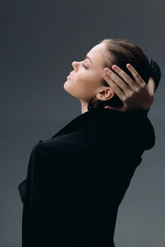Profile of a calm woman with closed eyes and dark clothing against a neutral background, expressing peace and contemplation.