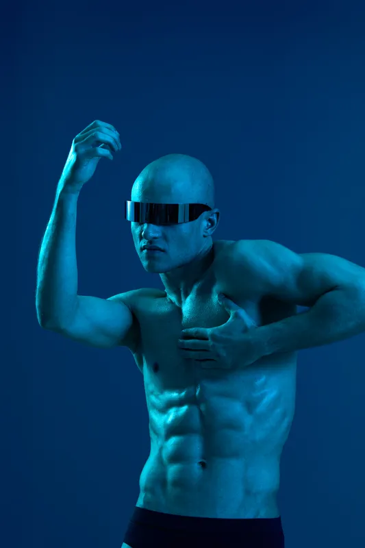 Muscular man posing dramatically in blue light, showcasing strength and confidence. Ideal for fitness and fashion themes with a futuristic touch.