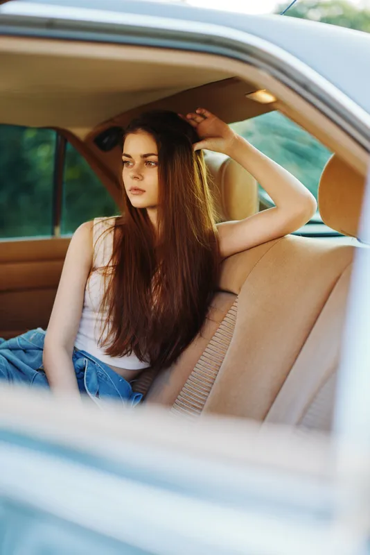 Thoughtful young woman with long hair sitting in a vintage car interior, expressing a sense of nostalgia and reflection in a relaxed moment during the day.