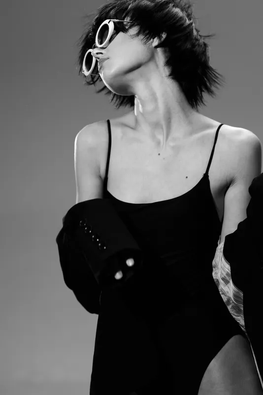 Stylish woman wearing sunglasses in black and white portrait with modern outfit and confident pose.