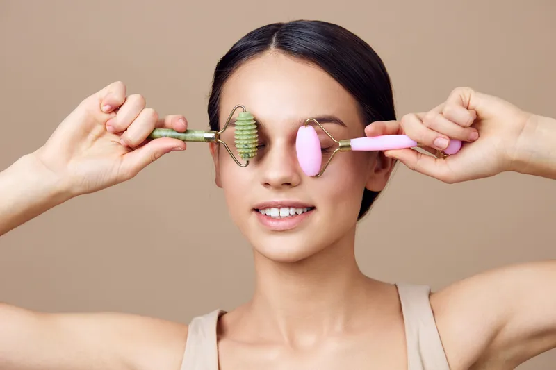 Young woman with facial rollers showcasing skincare routine, promoting healthy skin and beauty treatment concepts in neutral tones