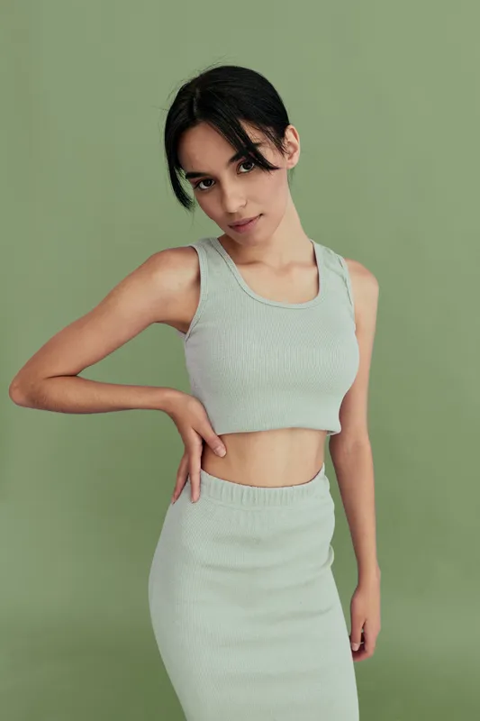 young woman wearing light green sleeveless crop top and skirt standing against soft green background in stylish casual outfit