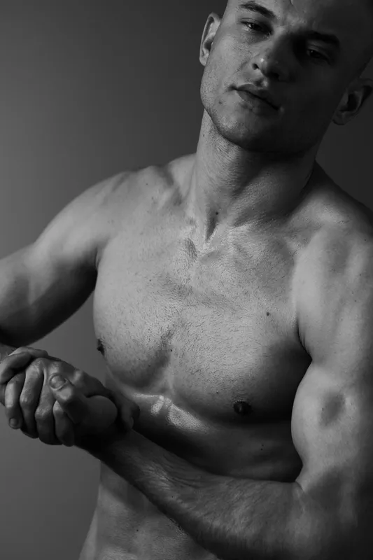Black and white portrait of a muscular man showcasing strength and confidence, highlighting his defined features and posture in an artistic manner.