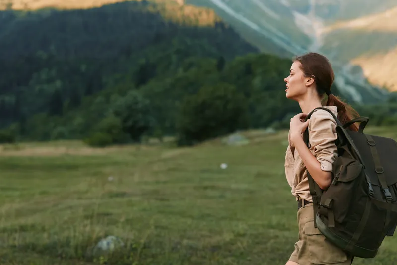 Woman hiking along a meadow trail with a backpack, enjoying nature and fresh air, exploring a mountain landscape, embodying outdoor lifestyle and personal adventure