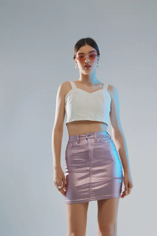 Young woman in a white crop top and shiny purple skirt poses confidently against a plain background. Concept for woman beauty fashion and modern style.