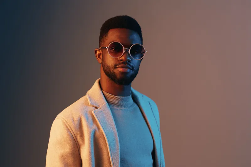 Stylish young African man in a beige blazer and sunglasses, exuding confidence against a gradient background, perfect for fashion and lifestyle concepts