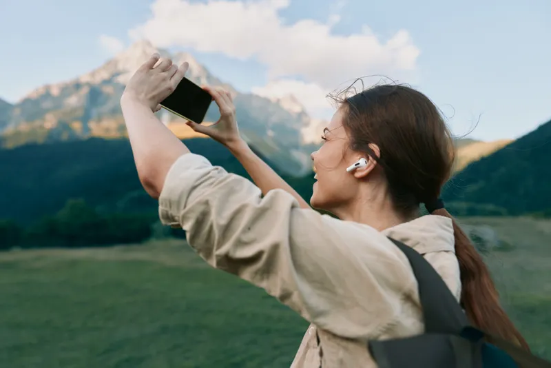 Woman outdoor selfie with mountains and nature, travel vibe, backpack and smartphone in hand, lifestyle moment of adventure outdoors
