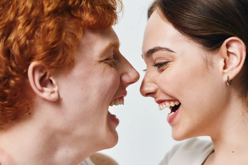 Portrait of smiling happy young man and woman looking at each other, laughing and enjoying joyful moment with closeup on faces and natural emotion in casual setting.