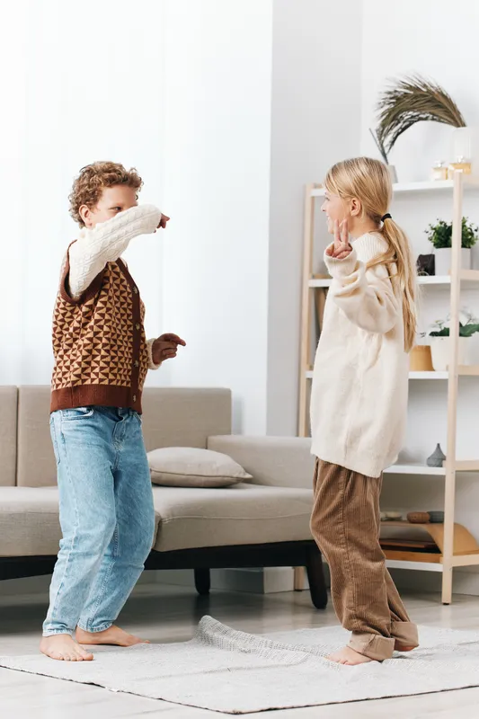 Authentic scene of playful home life featuring school-age children dancing and laughing together, capturing spontaneous movement and everyday lifestyle in a warm, inviting setting.