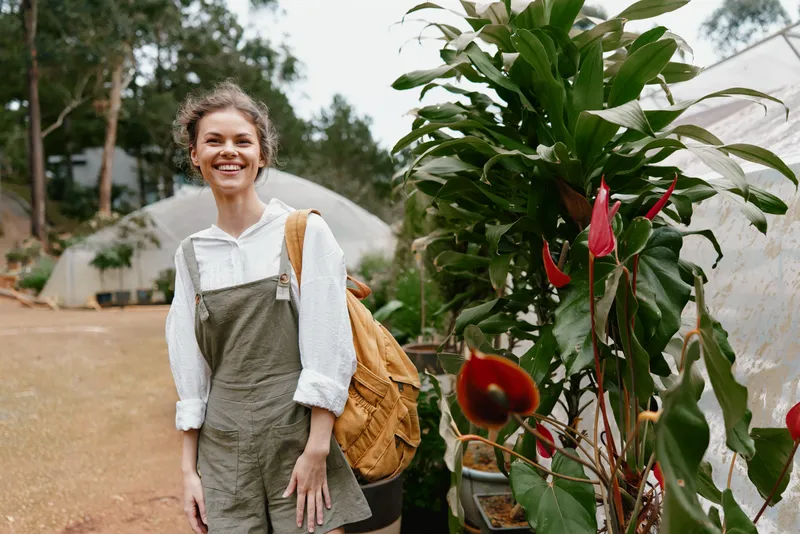 Smiling young woman in casual outfit posing outdoors near lush greenery, exuding joy and confidence in a natural setting