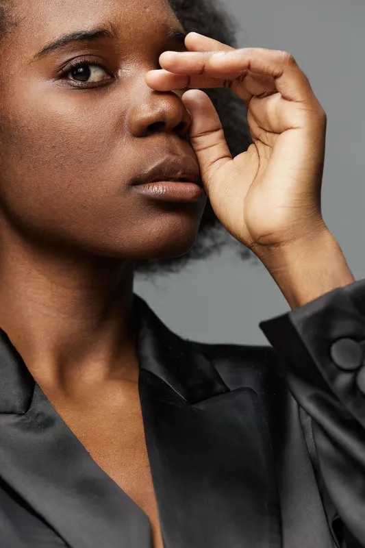 Portrait of a young Black woman with natural hair, wearing a stylish black silk blouse, expressing contemplation against a neutral gray background