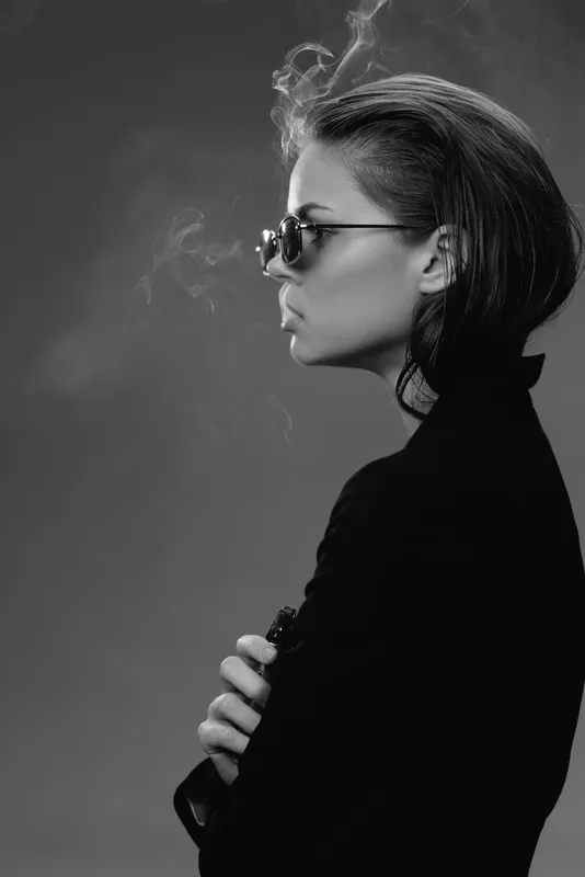 Black and white profile of a stylish woman smoking, wearing sunglasses and a dark outfit with a moody, elegant atmosphere.