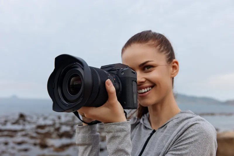 Young female photographer capturing nature moments with a DSLR camera by the seaside, showcasing joy and creativity in a vibrant outdoor setting