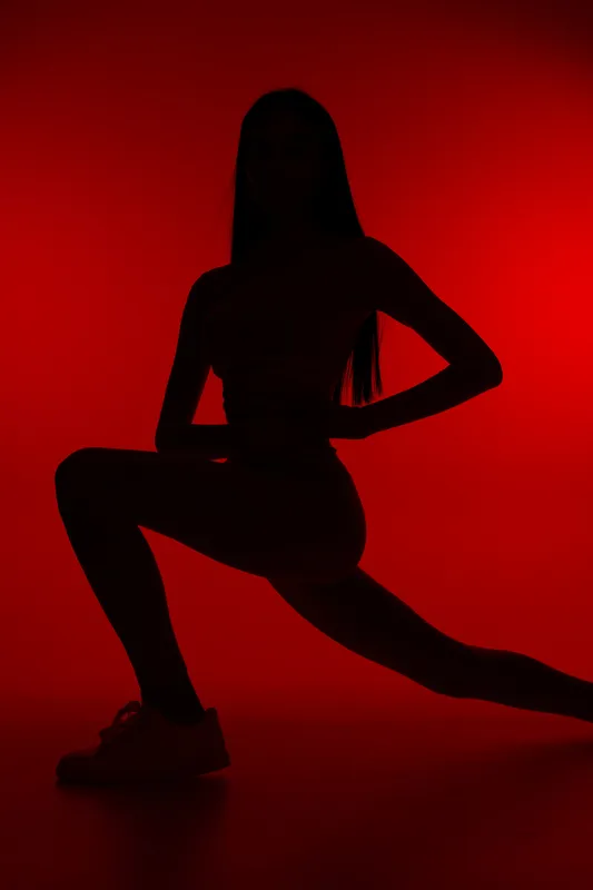 Woman sport fitness silhouette performing a deep lunge exercise against a vivid red background, showcasing strength, balance, and focus in a minimalistic studio setting.