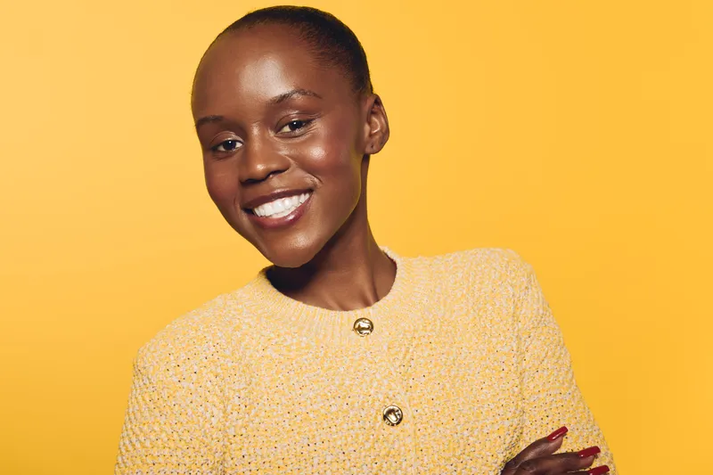 Smiling dark skinned African woman with smooth skin wearing yellow textured sweater stands against yellow background. Concept of beauty, confidence, fashion, and positive mood in studio lighting.