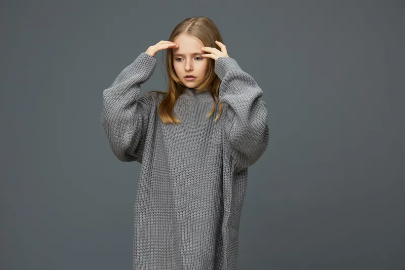 A young girl in a cozy grey oversized sweater, showcasing emotions of stress and contemplation against a muted background Perfect for discussions on mental health