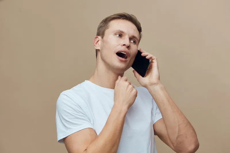 Smiling man talking on mobile phone casual clothing indoor beige background cheerful express happiness communication concept
