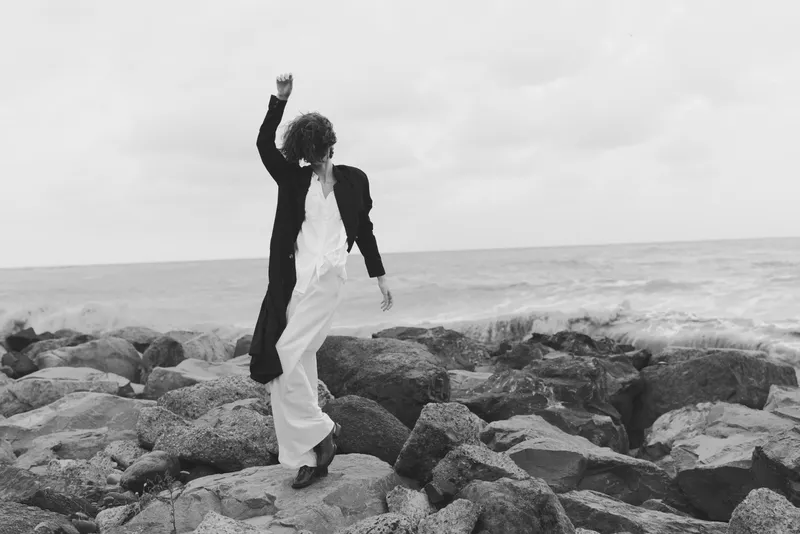 Dancer on rock sea pose with jacket movement in monochrome fashion and motion, capturing coast energy and bold balance against rugged shore and open water