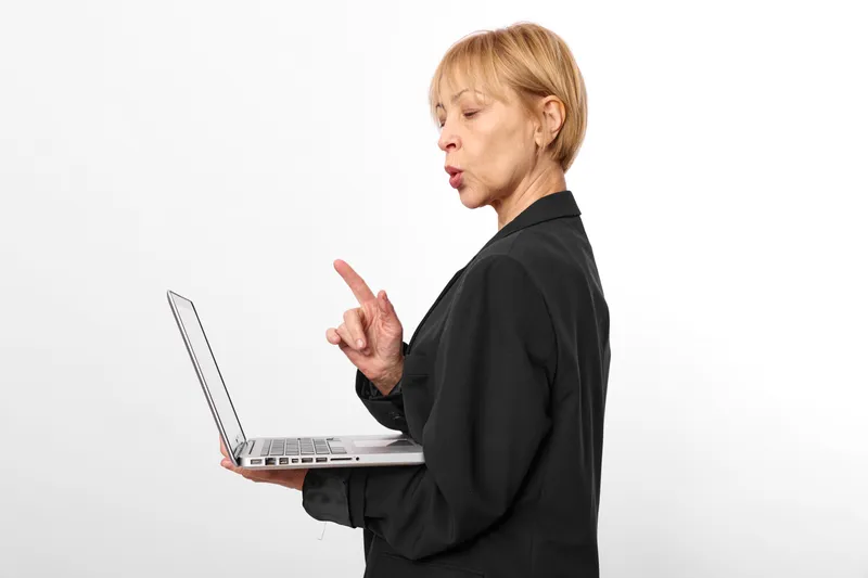 Woman with laptop in office studio on white background, black jacket, business communication with hand gesture, focused sideways look, modern technology, thoughtful expression, copy space