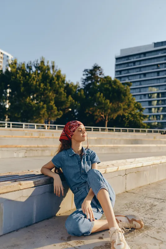 lifestyle woman in modern boho-western denim street style relaxing outdoors under sunlight with film color tones and casual summer vibe