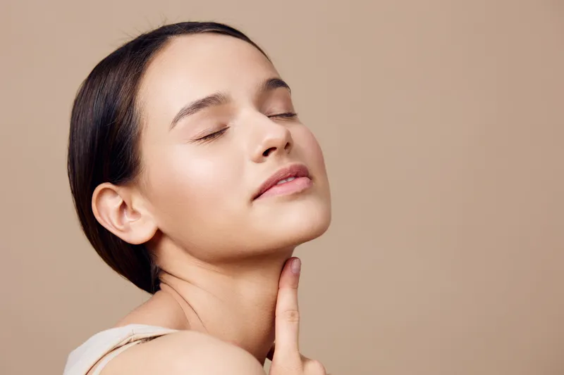 Young woman with a serene expression on a neutral background, showcasing natural beauty and skincare Reflects self care and confidence