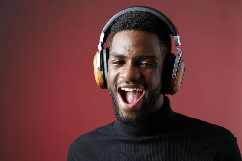 Happy young Black man enjoying music with headphones on a red background, expressing joy and excitement through his smile