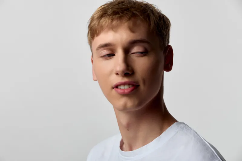 Young man, face expression closeup casual studio lighting simple background white tee, thoughtful relaxed emotion mood, candid contemporary photography with natural realism lifestyle