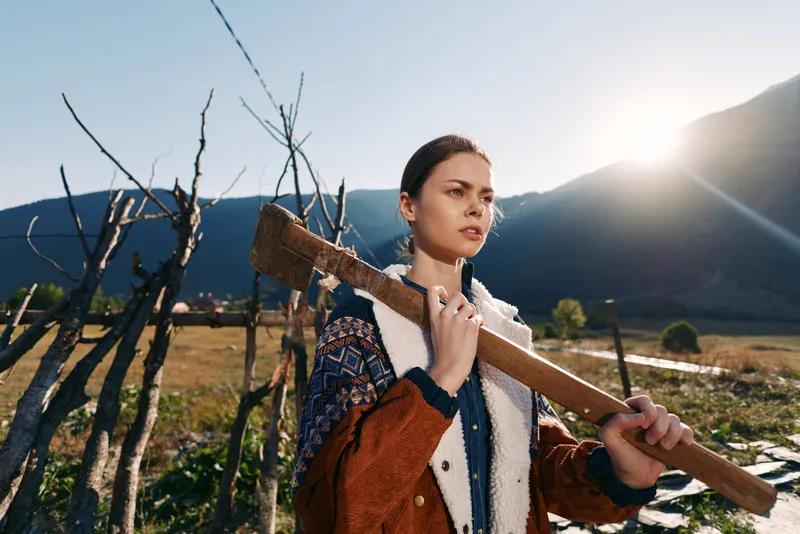 woman plank rural mountains fence sunlight portrait of young female carrying a wooden beam on her shoulder in countryside farm outdoor scene, rustic jacket and determined expression