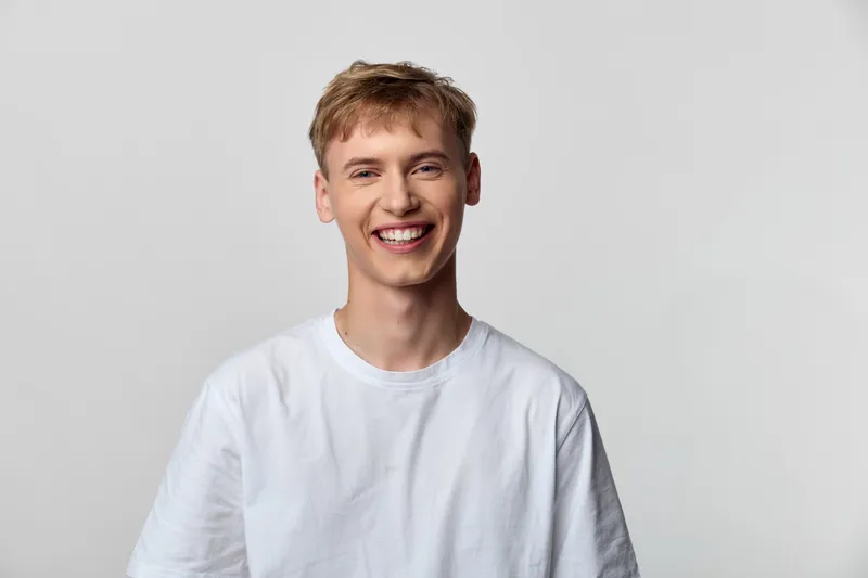 Smiling young man in a white tshirt facing the camera, casual studio image with cheerful expression, bright lighting, relaxed stance, approachable vibe, modern clean background