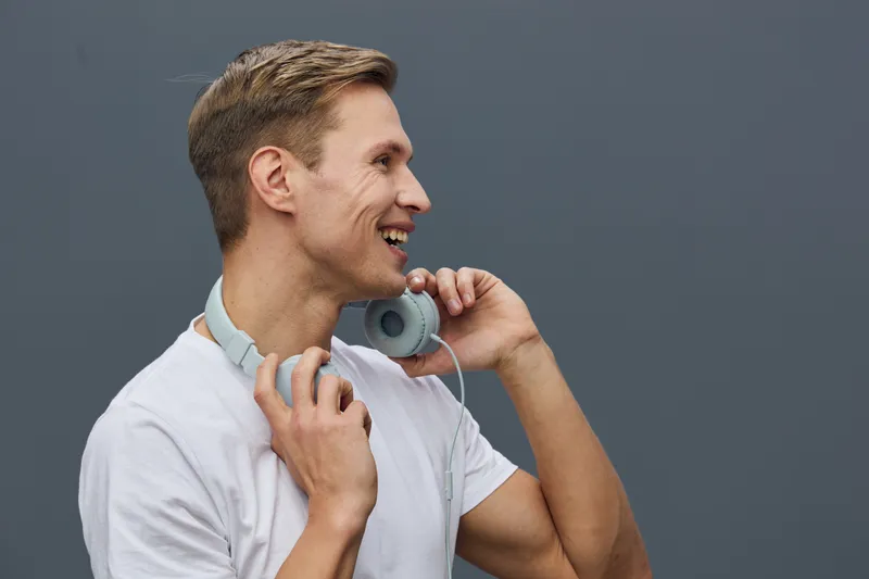 smiling young caucasian man with headphones casual white t-shirt looking side listening music isolated on gray background concept digital detox mental health gadgets