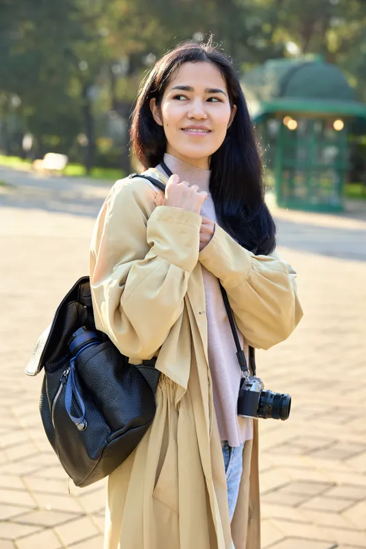 Woman with backpack and camera in a sunlit park, candid moment capturing light, fashion inspired outfit, outdoor lifestyle scene showcasing travel vibes and everyday exploration