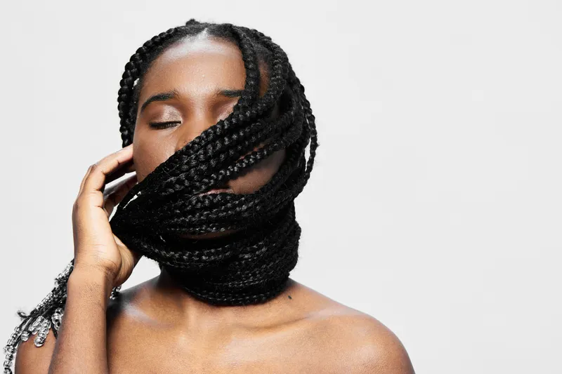 Young Black woman with braided hair, showcasing confidence and serenity through a striking portrait against a minimalist background