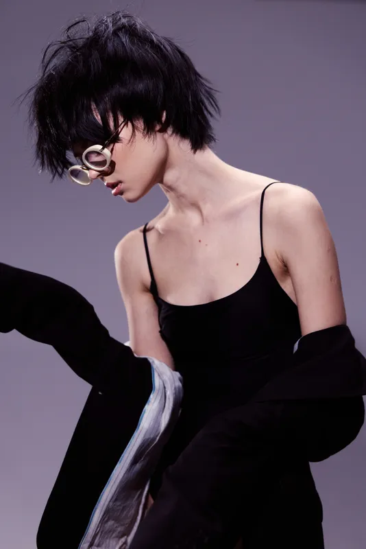 Stylish woman with short black hair wearing sunglasses and black outfit in fashionable pose.