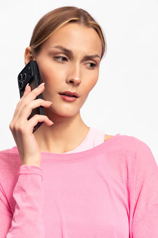 Young woman in pink sweater talks on smartphone with serious expression against white background. Concept for communication, technology, and modern lifestyle.