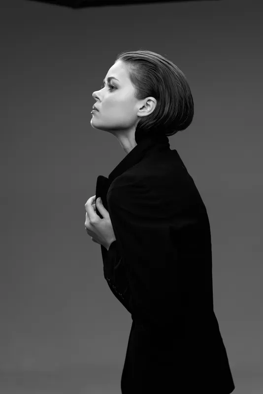 Black and white portrait of a young woman with short hair wearing a dark blazer in a contemplative pose.