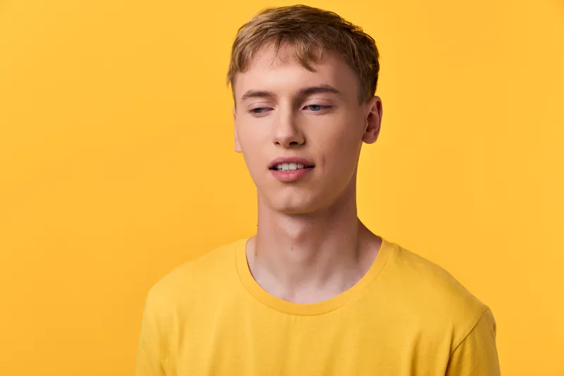 Young man in a bright yellow shirt against a bold yellow backdrop, showcasing casual style, relaxed mood and soft studio lighting for fashion or lifestyle use.