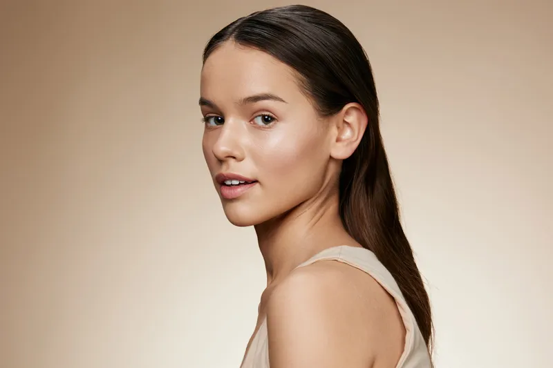 Elegant young woman with natural makeup and long hair showcasing a serene expression against a soft beige background, perfect for beauty and fashion concepts