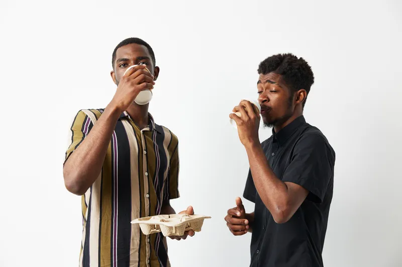 Two young African American men enjoying drinks together, showcasing friendship and joy. They wear stylish outfits and share a light-hearted moment, creating a vibrant atmosphere.