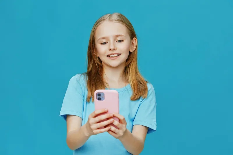 Happy girl with smartphone on a bright blue background, wearing a casual light blue t shirt, expressing joy and excitement in a colorful and vibrant setting