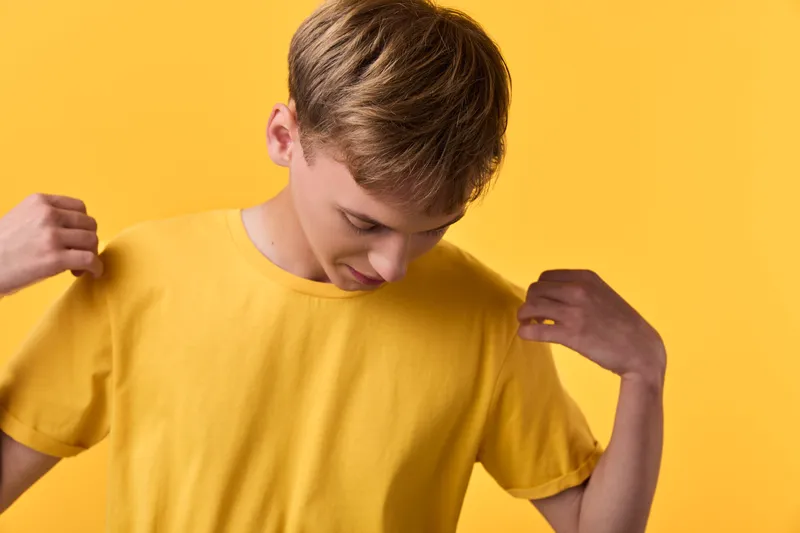 Young boy in a bright yellow shirt adjusts his tee against a matching yellow backdrop, casual studio shot, relaxed style, simple composition, warm color harmony.