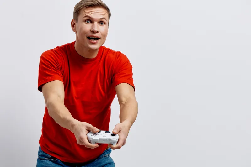 excited young caucasian man in red t-shirt playing video game holding wireless controller isolated on white background digital entertainment concept