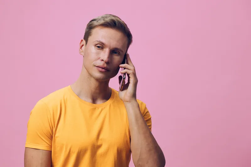 thoughtful man talking smartphone wearing orange t-shirt look side pink background digital communication concept
