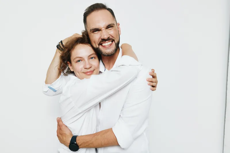 A professional man and colleague share a warm moment of success, showcasing confidence and teamwork against a solid color background. Emotions include happiness, pride, and support, reflecting a